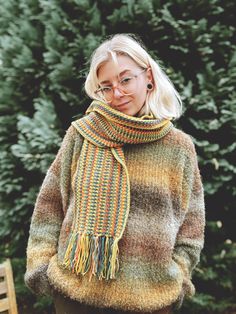 a woman standing in front of a tree wearing a multicolored sweater and scarf