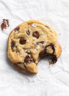 a half eaten chocolate chip cookie sitting on top of white paper with one bite taken out