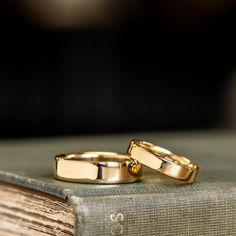 two gold wedding rings sitting on top of an old book