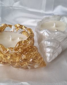 two candles sitting next to each other on a white cloth covered tablecloth with a golden candle holder in the middle