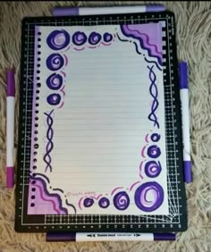 a notepad with purple and black designs on it, sitting on a carpet next to two pens