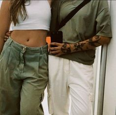 two people standing next to each other with tattoos on their arms and stomachs, one holding a cell phone