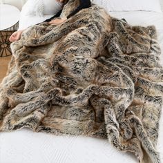 a woman laying on top of a bed covered in a furry animal fur throw blanket