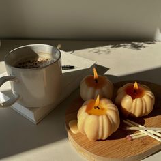 three pumpkin shaped candles on a wooden tray next to a cup of coffee and chopsticks