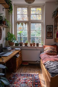 a bedroom with a bed, desk and plants in the window sill next to it