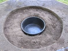 a black bowl sitting in the middle of a cement pit with dirt around it and grass behind it