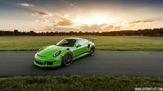 a green sports car parked on the side of a road in front of some grass