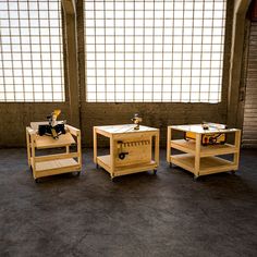 three wooden tables sitting next to each other on top of a cement floor in front of large windows