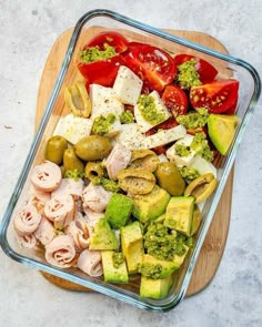 a glass dish filled with different types of vegetables and meats on top of a wooden cutting board