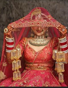 a woman in a red and gold bridal outfit with jewelry on her head, wearing a veil