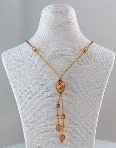 This romantic necklace features Murano glass beads in the following shapes: oval, leaves, cubes and coins.  The central bead measures 20mm (25/32 in.). It encases 24kt gold foil forming abstract patters that glitter in the presence of light.  The cubes also contain 24kt gold foil and measure 6mm (15/65 in.) This necklace is fully beaded with Czech gold-layered seed beads.  As always, the lobster closure and extender chain, 50mm (2 in.), are made of 14kt gold filled* materials. Measurement Conver Vintage Glass Necklaces With Oval Beads, Elegant Czech Glass Beaded Necklaces With Large Beads, Vintage Glass Necklace With Oval Beads, Elegant Czech Glass Beaded Necklace With Large Beads, Elegant Glass Necklaces With Faceted Beads, Elegant Necklace With Large Czech Glass Beads, Amber Beaded Necklace With Czech Glass, Elegant Glass Necklace With Faceted Beads, Amber Beaded Czech Glass Necklaces