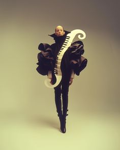 a woman is dressed in black and holding a giant white piano like instrument while standing against a gray background