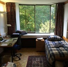 a bed room with a neatly made bed next to a desk and a large window