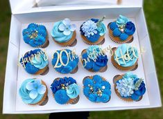 a box filled with blue cupcakes sitting on top of a grass covered field