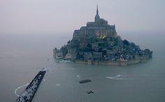 an island in the middle of water with boats floating on it's sides and people walking around