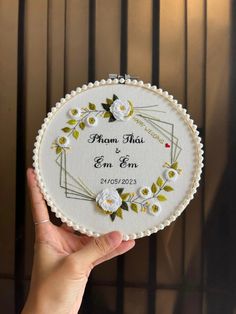 a hand holding a white embroidered wedding ornament with flowers and leaves on it