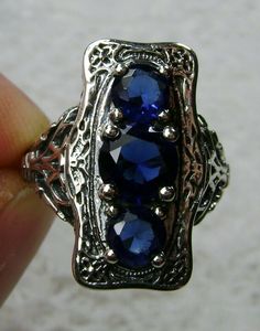 "Simulated Blue Sapphire Ring 3Stone Rectangle#60 Custom Made This is a lovely late Victorian era reproduction ring in solid sterling silver. The gorgeous filigree ring is set with 3 round-cut simulated blue sapphire gemstones. The 2 smaller blue sapphire gems are 4.5mm in diameter, and the center one is 6mm in diameter. This filigree setting is a casting from an actual Antique ring; notice the amazing etched band... The ring sits 3/4th\" (19mm) NS on the finger. The quality of the silver and ge Sapphire Three Stone Sterling Silver Ring, Blue Three Stone Sapphire Ring In Sterling Silver, Three Stone Sapphire Ring In Sterling Silver, Sterling Silver Sapphire Ring With Rectangular Stone, Sapphire Three Stone Ring Jewelry, Sterling Silver Three Stone Sapphire Rings, Blue Three Stone Sterling Silver Jewelry, Silver Three-stone Sapphire Jewelry, Silver Three Stone Rectangular Jewelry