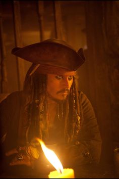 a man with dreadlocks and a hat on sitting in front of a lit candle