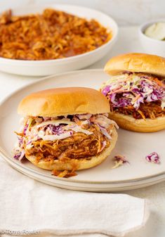 two pulled pork sandwiches with cole slaw on a plate next to a bowl of chili