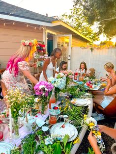 a group of women standing around a table with plates and flowers on top of it