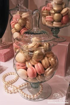 two glass containers filled with macaroons on top of a table next to pearls