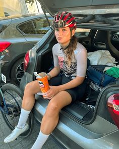 a woman sitting in the back of a car holding a drink and wearing a helmet