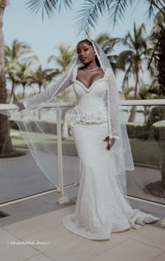 a woman in a wedding dress standing on a balcony with palm trees and buildings behind her