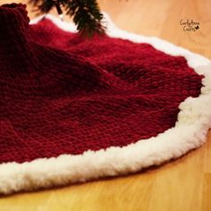 a red and white blanket sitting on top of a wooden floor next to a christmas tree