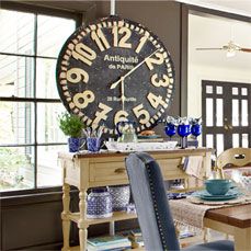 a large clock mounted to the side of a wall above a dining room table with blue chairs