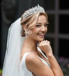 a woman wearing a bridal veil and tiara smiles at the camera with her hand on her chin