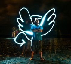 a man standing in the sand with his arms crossed and glowing lights behind him at night