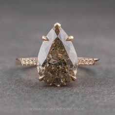 a pear shaped brown diamond ring with diamonds on the band and side stones in yellow gold