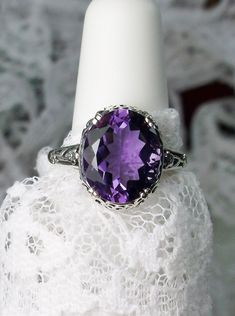 "Natural Purple Amethyst Ring Description Edward Design#70 (smaller version) MADE TO ORDER Inspired by Edwardian jewelry of the early 1900s, I now offer this lovely Antique reproduction ring in sterling silver. This gorgeous ring is set with a stunning 3.32ct Natural purple amethyst gemstone. This genuine amethyst has excellent color and clarity. The oval cut amethyst is 12mm (1/2th of an inch) Long by 10mm Wide (3/8th\"). The ring sits 6mm off the finger. The inside of the band s marked 925 for Classic Oval Gemstones For Wedding, Oval Purple Diamond Cut Jewelry, Purple Oval Diamond Cut Jewelry, Heirloom Oval Amethyst Ring With Accent Stones, Antique Oval Amethyst Ring With Center Stone, Classic Oval Gemstones For Anniversary, Oval Hallmarked Amethyst Ring In White Gold, Classic Oval Amethyst Ring With Accent Stones, Classic Oval Purple Gemstones