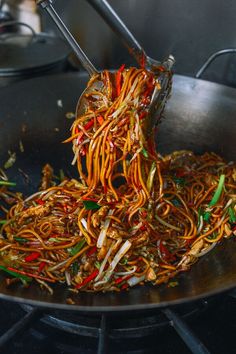 noodles being cooked in a wok with tongs on the top and stir frying