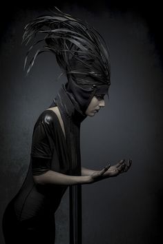 a woman with black feathers on her head and hands in front of a dark background