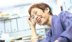 a woman sitting at a desk talking on a cell phone and laughing with her eyes closed