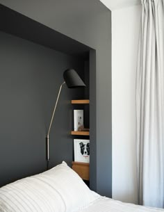 a white bed sitting under a black lamp next to a book shelf with pictures on it