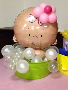 a balloon in the shape of a baby's head sitting on top of a bucket filled with balloons