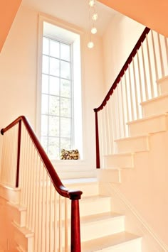 an empty staircase leading up to a bright window in a white room with wooden handrails