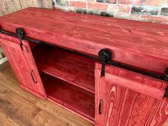 a red wooden entertainment center with sliding doors on the front and side, against a brick wall