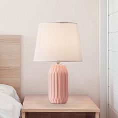 a pink lamp sitting on top of a table next to a bed