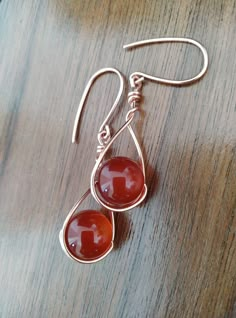 two red glass beads hang from silver earwires on a wooden table with a wood surface