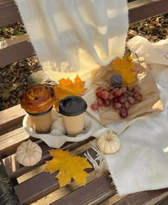 a wooden bench topped with fall leaves and cups of coffee