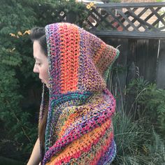 a woman wearing a multicolored crocheted shawl in front of a fence