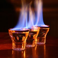 three shot glasses with blue flames in them on a table