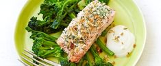 a green plate topped with broccoli and fish next to a fork on a white table