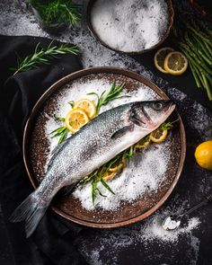 two fish are on a plate with lemons and asparagus next to it