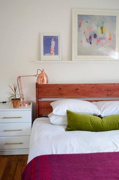 a bed with white sheets and pillows in a bedroom next to two pictures on the wall