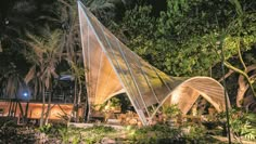 an outdoor area with trees and plants lit up at night in the background is a tent that looks like a sailboat