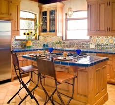 a kitchen with wooden cabinets and blue tile counter tops, two chairs at the island